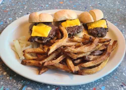 Three cheeseburger sliders on a plate with a side of crispy French fries.