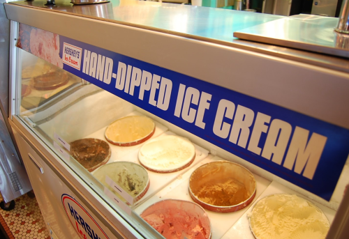 A display case of various hand-dipped ice cream flavors with a Hershey's sign above.