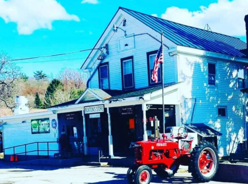 A red tractor parked in front of a white building with an American flag and a sign for "Bunting's Store."