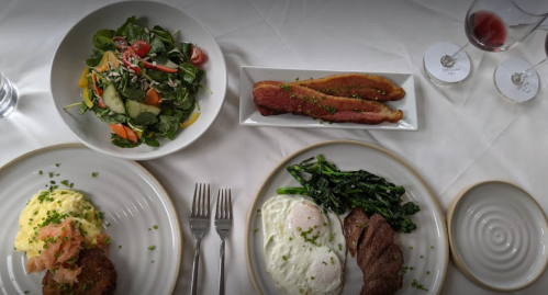 A table setting with a salad, smoked salmon, and a main dish of steak, asparagus, and creamy mashed potatoes.