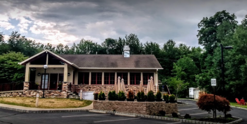 A stone-front building surrounded by greenery, featuring a porch and outdoor seating under umbrellas.