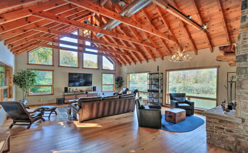 Cozy living room with wooden beams, large windows, and a view of nature, featuring comfortable seating and a TV.