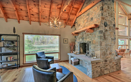 Cozy living room with stone fireplace, wooden beams, and large windows overlooking a scenic view.
