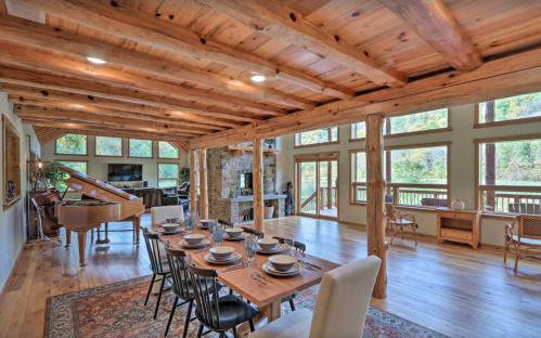 A spacious, rustic dining area with a wooden table set for dinner, surrounded by large windows and natural light.