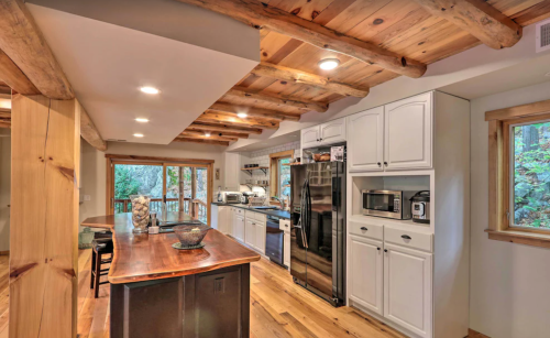 A modern kitchen with wooden beams, white cabinets, and a large island, featuring stainless steel appliances and natural light.