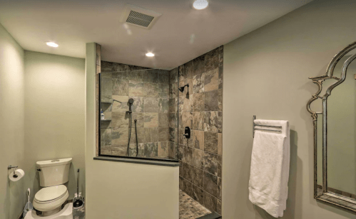 Modern bathroom featuring a shower, toilet, and elegant mirror with stone tile accents.