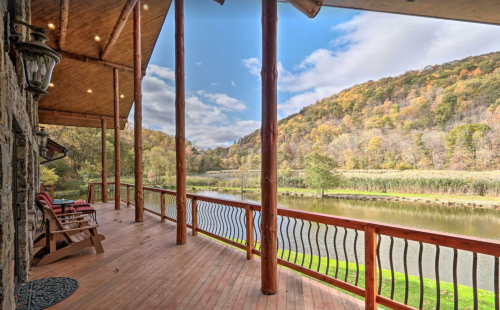 A scenic view from a wooden porch overlooking a river and autumn-colored hills under a partly cloudy sky.