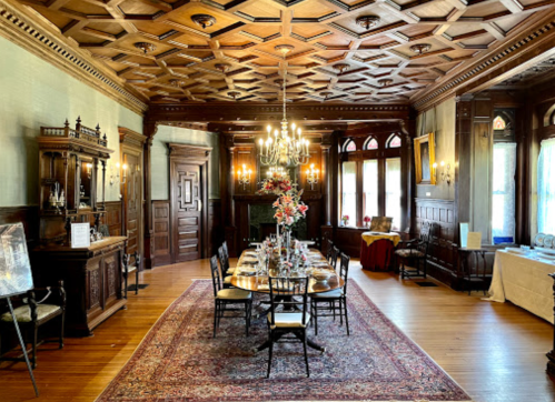 Elegant dining room with a coffered ceiling, chandelier, and a long table set for a meal, surrounded by ornate woodwork.