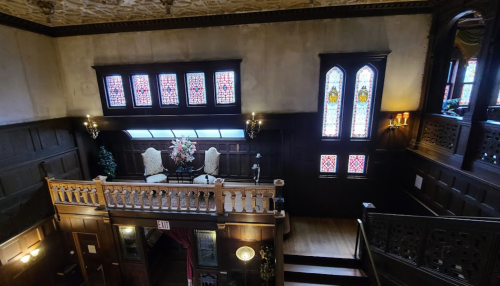 Elegant interior of a historic building featuring stained glass windows, wooden paneling, and ornate decor.