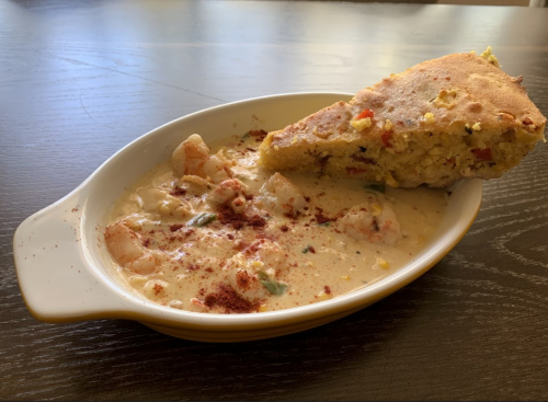 A dish of creamy shrimp stew with a slice of cornbread on the side, served in a white oval bowl.