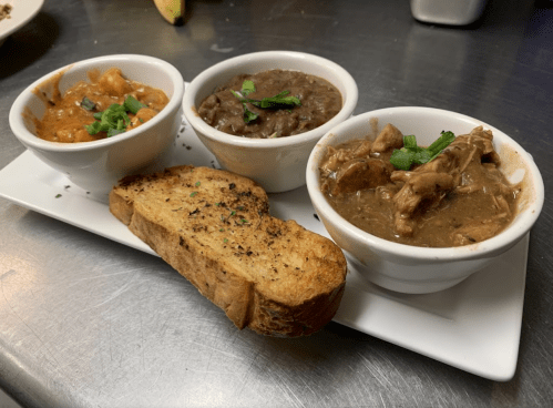 Three small bowls of different stews served with a slice of toasted bread on a white plate.