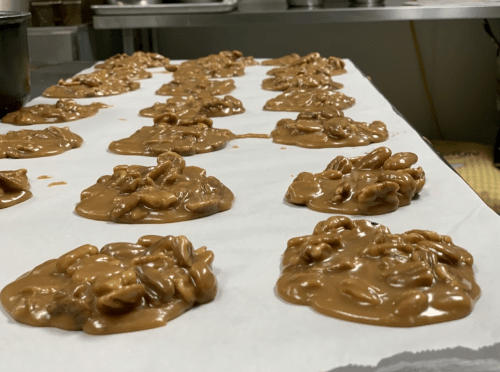 Clusters of caramel-coated nuts on parchment paper, cooling in a kitchen setting.