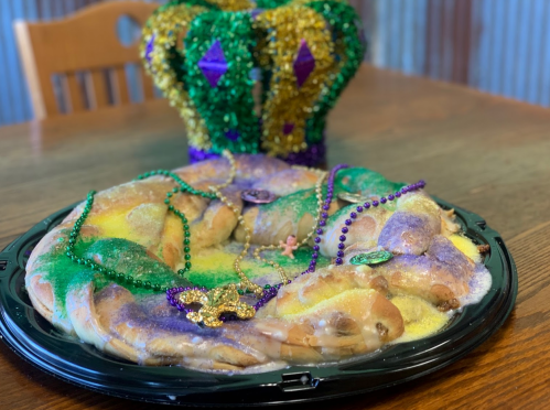A colorful king cake adorned with beads and a crown, set on a black platter against a wooden table.
