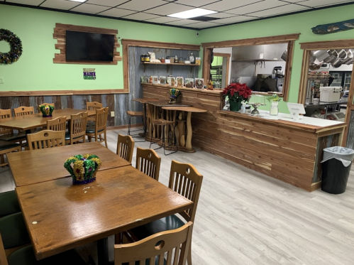 Cozy restaurant interior with wooden tables, green walls, and a service counter decorated with plants and holiday decor.