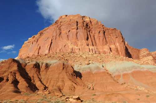 A towering red rock formation under a blue sky with scattered clouds, showcasing layered geological textures.