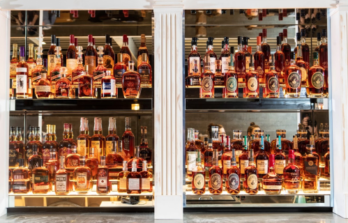 A display of various whiskey bottles on shelves, reflecting light in a stylish bar setting.
