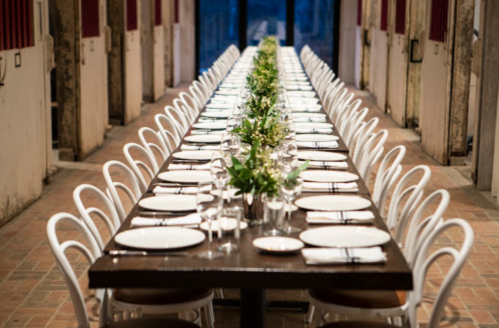 A long dining table set for a meal, adorned with greenery, in a spacious, elegant venue.