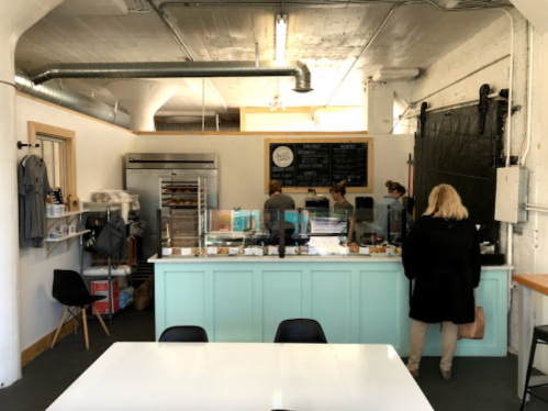 A cozy café interior with a light blue counter, shelves of baked goods, and customers interacting with staff.