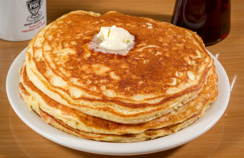A stack of golden pancakes topped with a pat of butter, served on a white plate with syrup in the background.