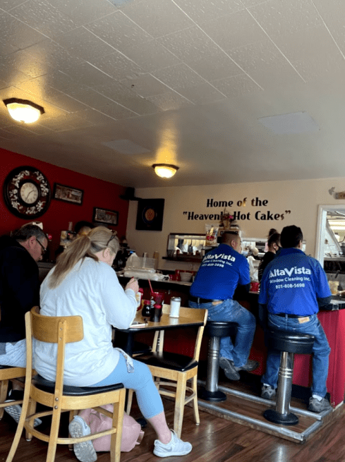 A cozy diner scene with patrons seated at the counter and tables, enjoying meals in a warm, inviting atmosphere.