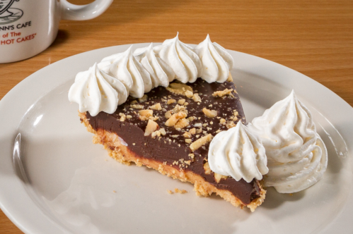 A slice of chocolate pie topped with whipped cream and crushed nuts, served on a white plate.