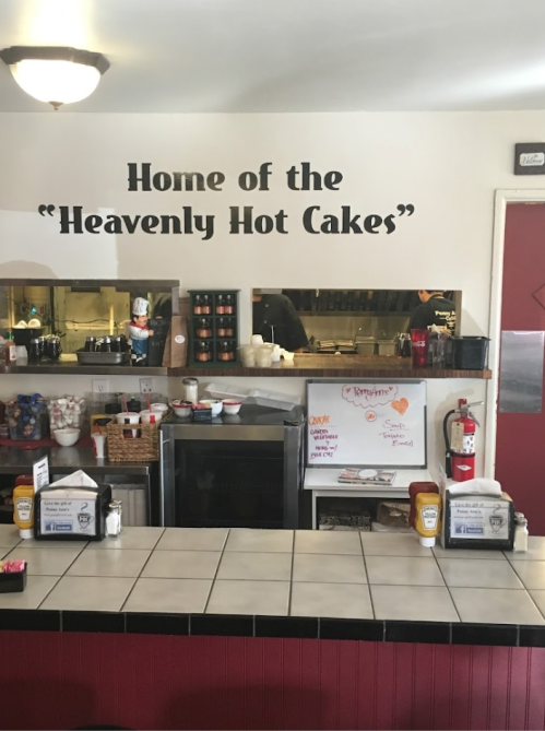 Interior of a diner with a sign reading "Home of the 'Heavenly Hot Cakes'" above a counter and kitchen area.