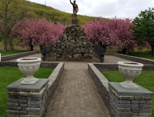 A stone monument with a statue atop, surrounded by blooming pink trees and landscaped pathways.