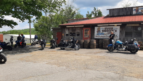 A group of motorcycles parked outside a rustic building with a red roof and a sign that reads "Your Farmer's."