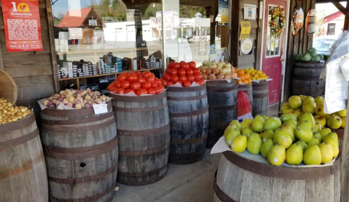 A rustic market display with barrels filled with colorful fruits and vegetables outside a shop.