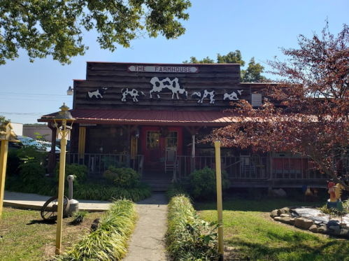 A rustic building with a red roof and cow decorations, surrounded by greenery and a clear blue sky.