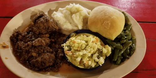 A plate of meatloaf with gravy, mashed potatoes, coleslaw, green beans, and a dinner roll on a red table.