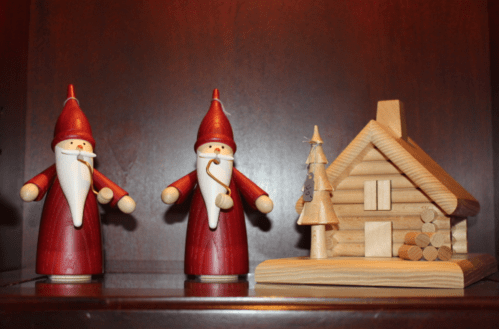 Two wooden Santa figures with red robes and a small wooden cabin with a tree beside it, displayed on a shelf.