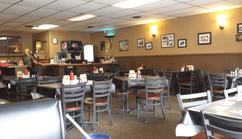 A spacious restaurant interior with empty tables, a bar area, and framed photos on the walls.
