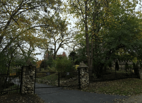 A gated entrance surrounded by trees and autumn leaves, leading to a distant, stately building.