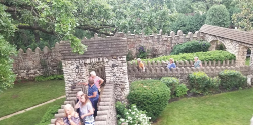 A group of people exploring a stone garden with walls and greenery, surrounded by trees.