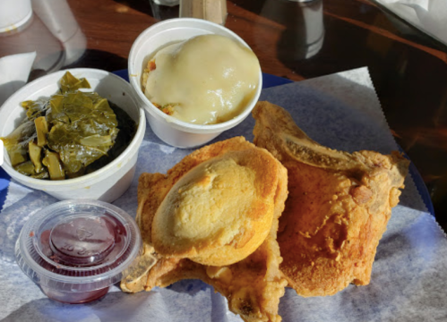A plate featuring two pieces of fried chicken, collard greens, and a side of mashed potatoes with gravy.