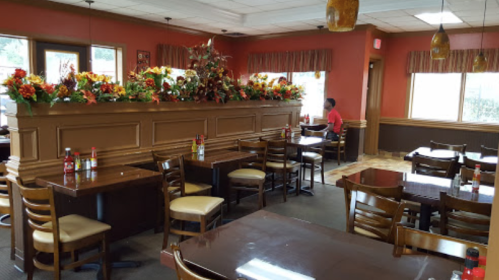 Cozy restaurant interior with wooden tables, chairs, and floral decorations along the walls. A diner is seated in the background.