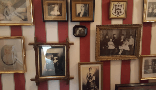 A wall adorned with various vintage framed photographs, featuring portraits in ornate frames against red and white stripes.