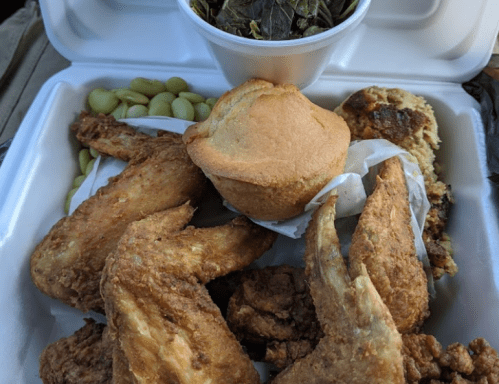 A takeout container filled with fried chicken, cornbread, collard greens, and lima beans.