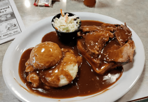 A plate of sliced meat with gravy, mashed potatoes, and coleslaw on the side.