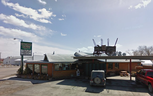 A rustic café with a wagon on the roof, surrounded by a parking area and blue sky.
