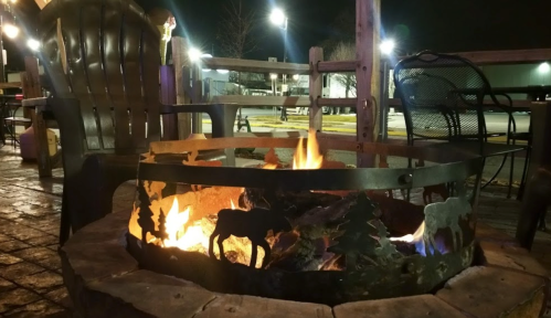 A cozy fire pit with a metal design, surrounded by chairs, glowing warmly in a nighttime setting.