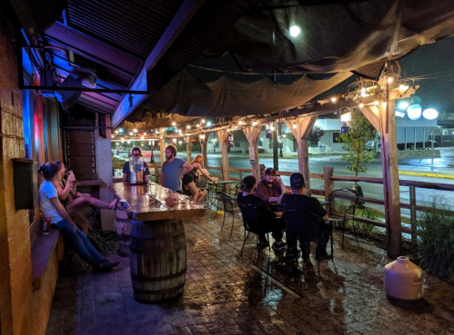 A cozy outdoor bar scene with patrons sitting under string lights, enjoying drinks on a rainy evening.