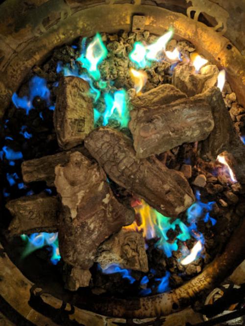 A close-up of glowing logs in a fire pit, surrounded by vibrant blue and green flames.