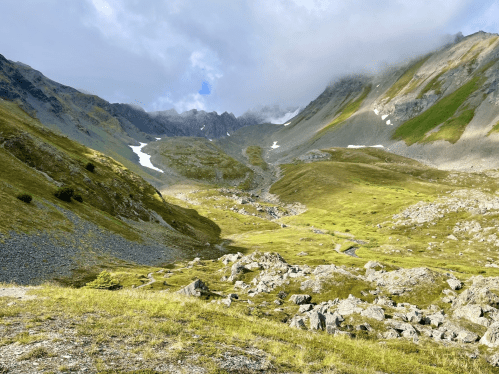 A scenic mountain landscape with green hills, rocky terrain, and a clear blue sky.