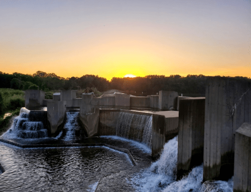 A serene sunset over a waterfall with concrete structures, surrounded by lush greenery.