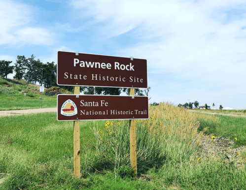 Sign for Pawnee Rock State Historic Site and Santa Fe National Historic Trail, surrounded by green grass and blue sky.