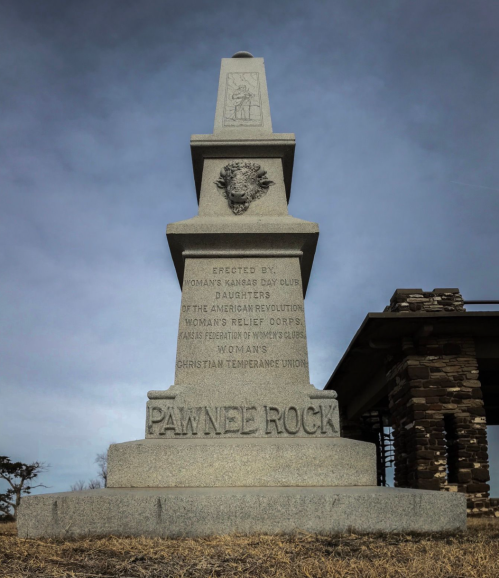 A stone monument with inscriptions, dedicated to women's organizations, set against a cloudy sky.