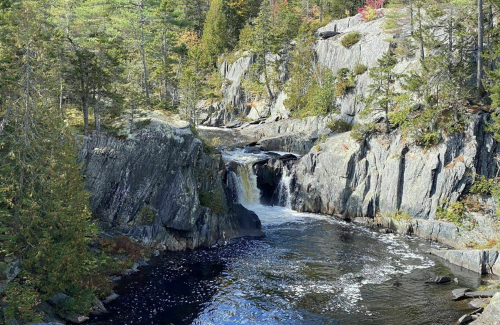 A serene river flows through rocky terrain, surrounded by trees and autumn foliage.