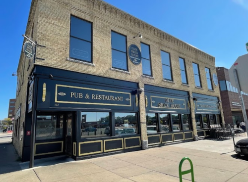 Exterior of a brick pub and restaurant with large windows and a sign, set against a clear blue sky.